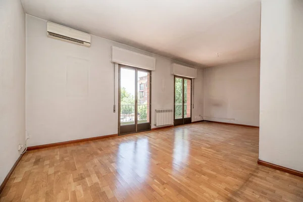 Empty living room of a residential house with oak parquet floor, two large aluminum and glass balconies and air conditioner on the wall