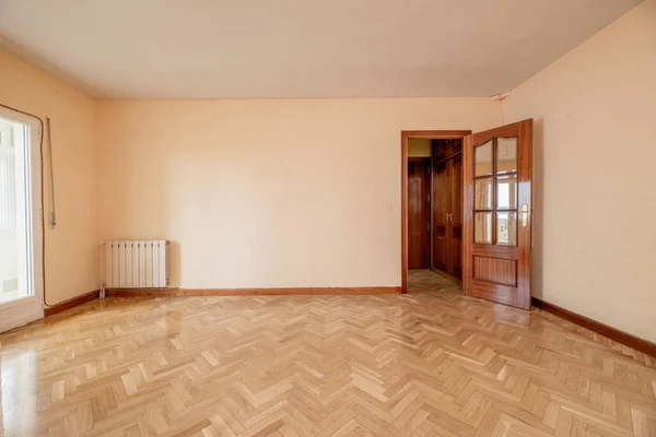 Empty room with white aluminum window, radiator in a niche, varnished French oak parquet and soft pale pink painted walls