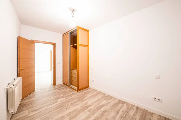 Renovated room with built-in wardrobe with sliding doors in cherry wood color, interior chest of drawers, matching front door and aluminum radiator on the wall