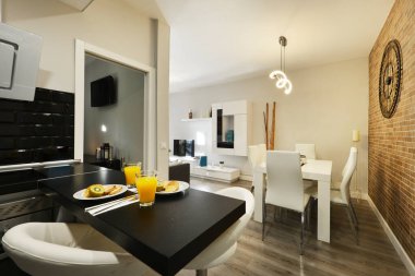 Küçük daire açık mutfak, siyah ahşap masa, beyaz tabure, tuğla aksan duvar ve beyaz ahşap yemek masası.