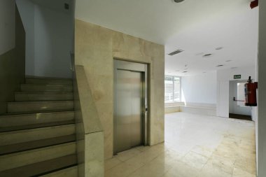 Asansörü ve mermer merdivenleri olan bir apartmanın salonu.