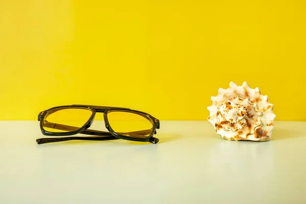 コンチシェルの横に黄色のレンズと黒のサングラス — ストック写真
