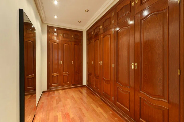 Dressing room of an apartment with large closets with reddish wood doors, mirrors and wooden floors
