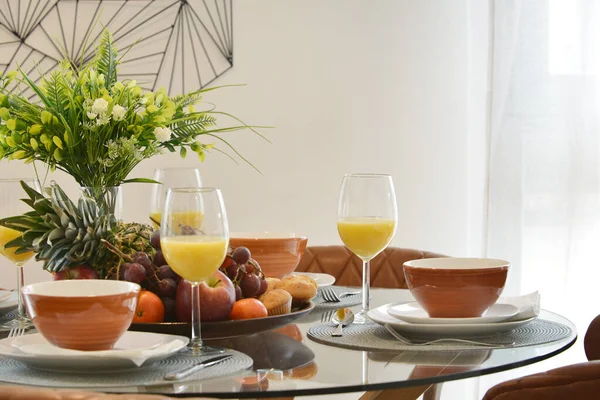 A circular glass dining table with trays of fruit and glasses of orange juice