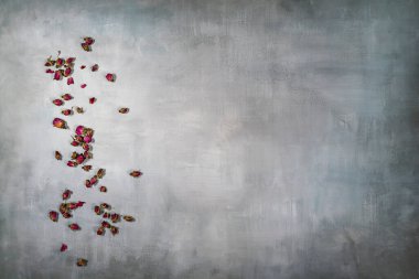 Soluk gri arka planda küçük kurumuş çay gülleri ve izler.