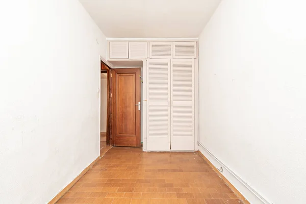 Small empty bedroom with white fitted wardrobe with Venetian style doors