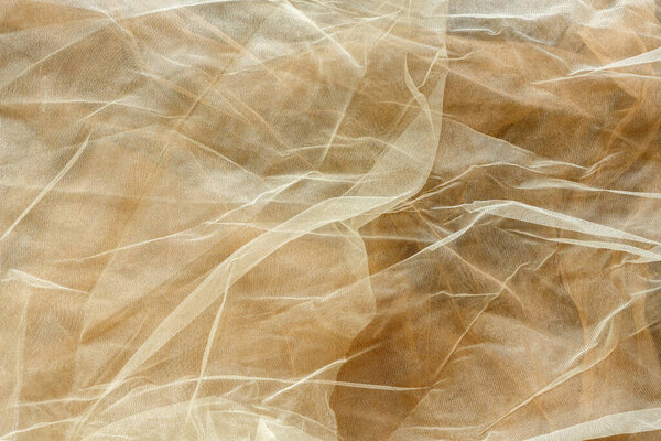 Subtle background of semi-sheer light cream colored tulle fabric with a visible pattern and some wrinkles