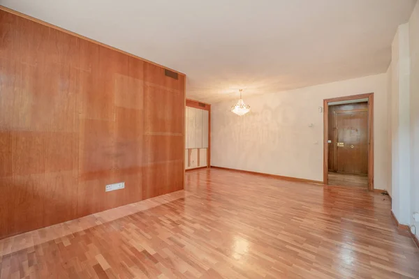 Empty room with a wall covered with a wooden varnish mural in a color that matches the parquet floors