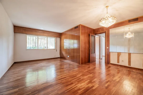 Empty room with one wall covered with a wood varnish mural in a color that matches the parquet floors, another with mirrors and a crystal chandelier on the ceiling