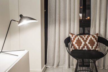 Beyaz perdeli bir pencerenin yanında okuma alanı olan kiralık bir evde dekoratif detaylar.