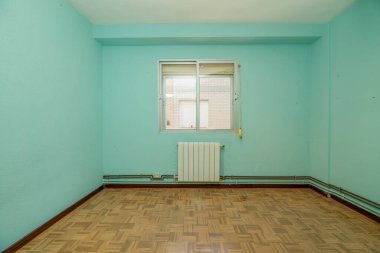 Mütevazı nitelikli, mavi boyalı duvarlar ve beyaz alüminyum radyatörle inşa edilmiş eski bir dairede boş bir oda.