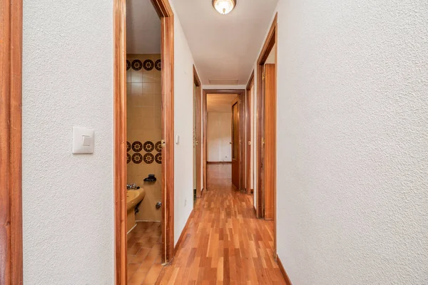 Corridor of an empty urban house with reddish wooden floors with access to several rooms and walls painted in white gotelet