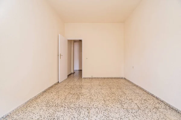Empty room in old apartment built with modest qualities, white painted walls, white door and terrazzo floors