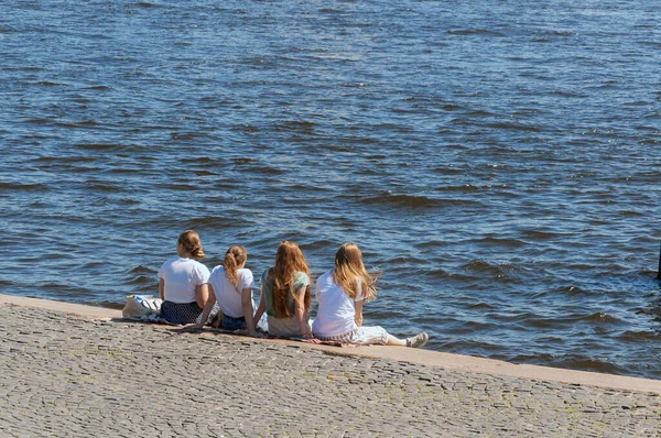 Dört genç kız arkadaş gün boyunca sırtüstü uzanan bir şehir nehrinin kıyısında yan yana oturuyorlar.