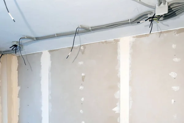 Tavan boyunca uzanan kıvrımlı bir elektrik kablosu. Duvarlar alçıpanla kaplı. Kuru sıva. Duvarlar dolu..