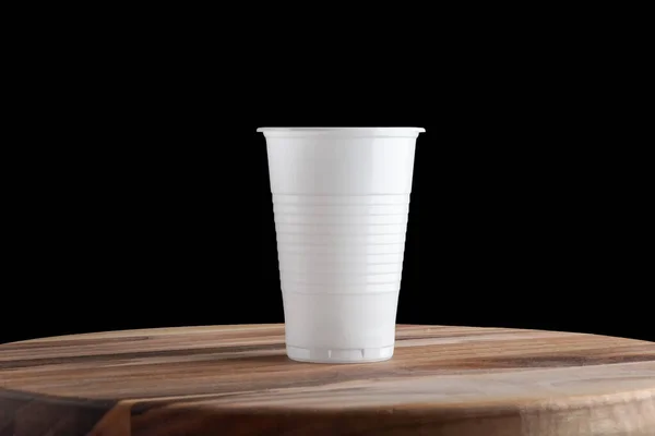 Taza desechable de plástico blanco sobre fondo negro y soporte de madera. Aislar — Foto de Stock