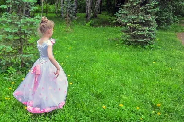 Pembe gül yapraklı beyaz prenses elbiseli küçük bir kız yeşil bir parkta yürüyor. Arkadan bak..