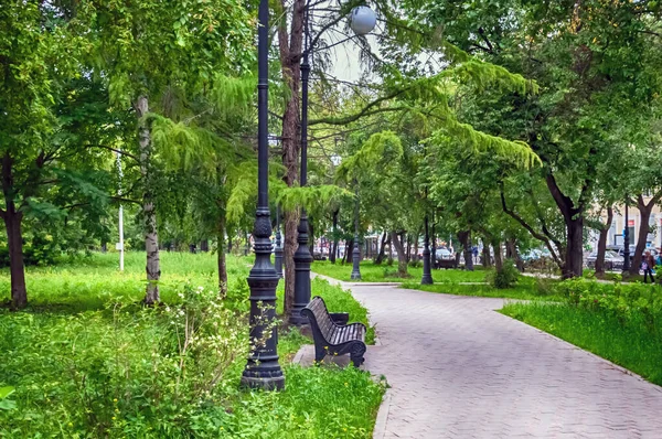 Sokak arasında sokak lambaları olan boş bir bank. Yaz. Gün.