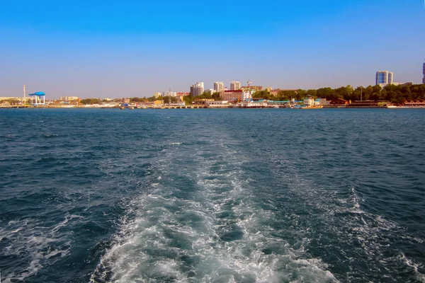 Limandan denize giden bir geminin izleri, şehir manzarasının arka planına karşı.