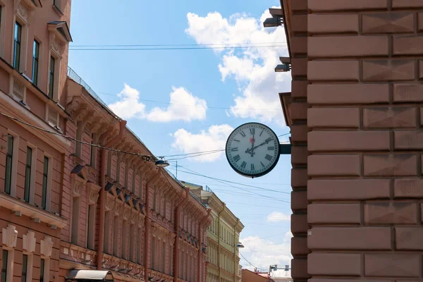 Bir binanın duvarında, bulutlu mavi gökyüzünün arka planına asılı duran yuvarlak bir sokak saati var.