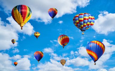 Mavi arka planda beyaz bulutlu renkli balonlar.