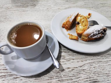 Masanın üzerinde beyaz bir fincan kahve ve çeşitli kekler..