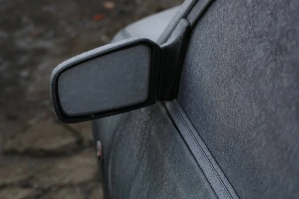The side glass and seals, the left rear-view mirror and its body, the direction indicator, the fender and the hood from the mazda 121 DB car, black-green, are sprinkled with the first frost. 