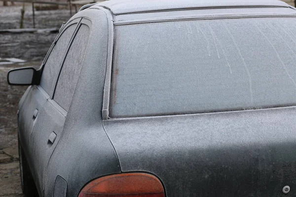 The side glass and seals, the left rear-view mirror and its body, the direction indicator, the fender and the hood from the mazda 121 DB car, black-green, are sprinkled with the first frost. 