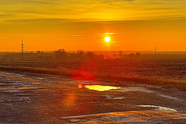 Dawn. Frosty morning in the orange rays of the rising sun. Plowing, frozen puddles, high-voltage wires, potholes on a provincial road, private houses