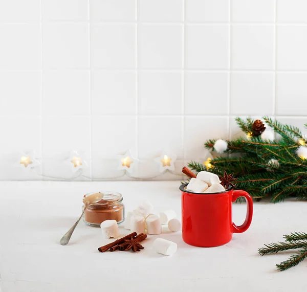 Sıcak çikolatalı kırmızı kupa, marşmelovlu ve mutfaktaki beyaz masada baharatlar.