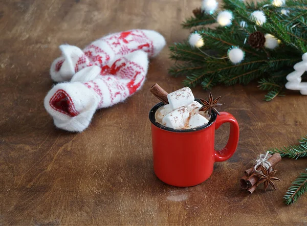 Sıcak çikolatalı kırmızı kupa marşmelov ve eldiven ve ağaç dalları ahşap masada.