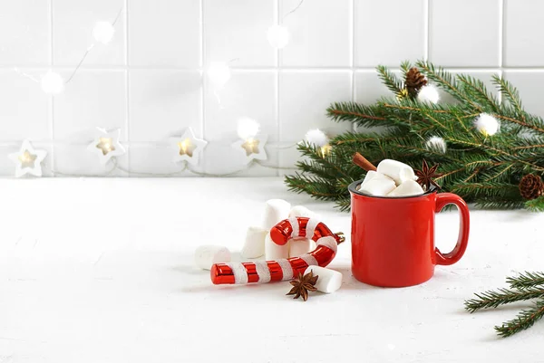 Sıcak çikolatalı kırmızı kupa, lokum ve beyaz mutfak masasında noel oyuncağı.