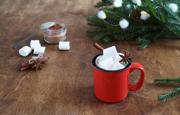 Marshmallow 'lu sıcak çikolatalı kırmızı kupa ve ahşap masada noel ağacı dalları.