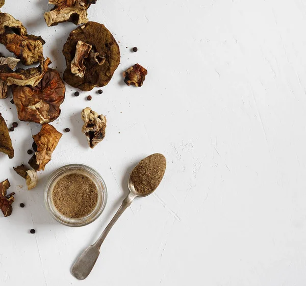 Cam bir kavanozda kurutulmuş porcini mantar tozu ve beyaz arka planda kurutulmuş mantarlar, üst manzara, kopyalama alanı
