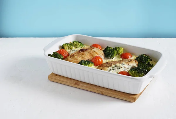 Brokoli ve domatesli fırınlanmış tavuk filetosu mavi duvar zemininde beyaz bir form, keto diyeti, kopyalama alanı