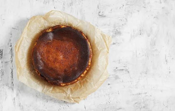 Beyaz zemin üzerinde fırınlanmış kağıt üzerinde ev yapımı Bask peynirli kekinin üst görünümü, boşluğu kopyala