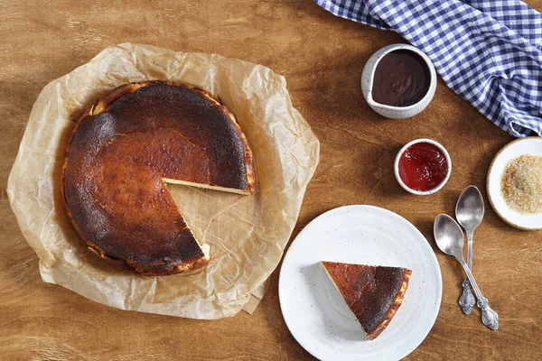 Lezzetli Bask peyniri yanmış, dilimlenmiş peynirli kek ve kırsal masada viyh çikolata ve reçel servis ediliyor.