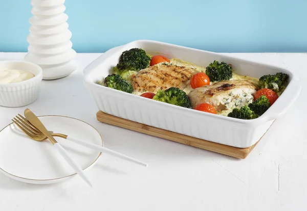 Brokoli ve domatesli fırınlanmış tavuk filetosu. Mavi duvar zemininde tabak ve çatal bıçak ile servis ediliyor. Keto diyeti, kopyalama alanı.