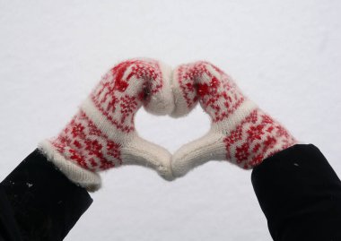 Karda kalp şeklinde beyaz ve kırmızı eldivenli kadınların elleri