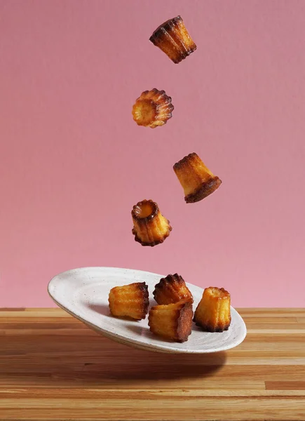 Canelle geleneksel bir Fransız hamur işi. Pembe arka plan ve ahşap masa üzerinde tabaktan uçuyor.