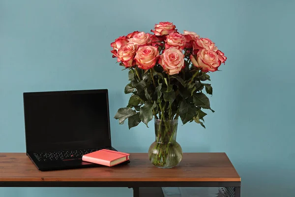 Kadınsı çalışma alanı, boş not defterli masa, klavye, şık ofis ve mavi arka planda pembe güller.