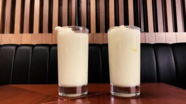 Two pino colada cocktails on a table in a bar with drinking straws