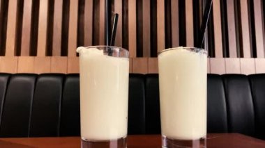 Two pino colada cocktails on a table in a bar with drinking straws