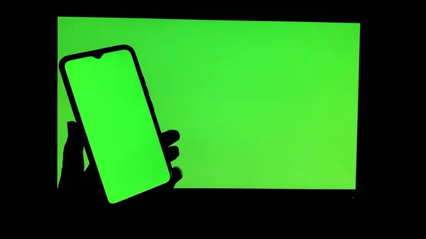 電子デバイス上のクロマキー 携帯電話やモニター 緑の画面と手が光が存在しない状態で画面をスクロール — ストック写真