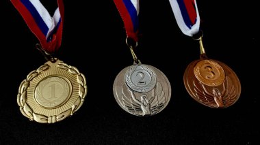 Altın, gümüş, bronz madalyalar ve siyah arka planda kupalar. İnsanların önünde gösterilen performanslar ve üst düzey spor başarıları için çok sayıda önemli ödül