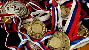 Altın, gümüş, bronz madalyalar ve siyah arka planda kupalar. İnsanların önünde gösterilen performanslar ve üst düzey spor başarıları için çok sayıda önemli ödül