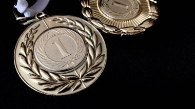 Altın, gümüş, bronz madalyalar ve siyah arka planda kupalar. İnsanların önünde gösterilen performanslar ve üst düzey spor başarıları için çok sayıda önemli ödül