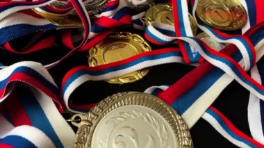 Altın, gümüş, bronz madalyalar ve siyah arka planda kupalar. İnsanların önünde gösterilen performanslar ve üst düzey spor başarıları için çok sayıda önemli ödül