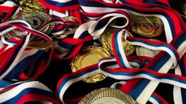 Altın, gümüş, bronz madalyalar ve siyah arka planda kupalar. İnsanların önünde gösterilen performanslar ve üst düzey spor başarıları için çok sayıda önemli ödül