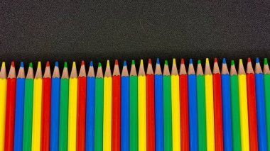 Siyah bir masanın üzerine uzanan parlak renkli kalemler.
